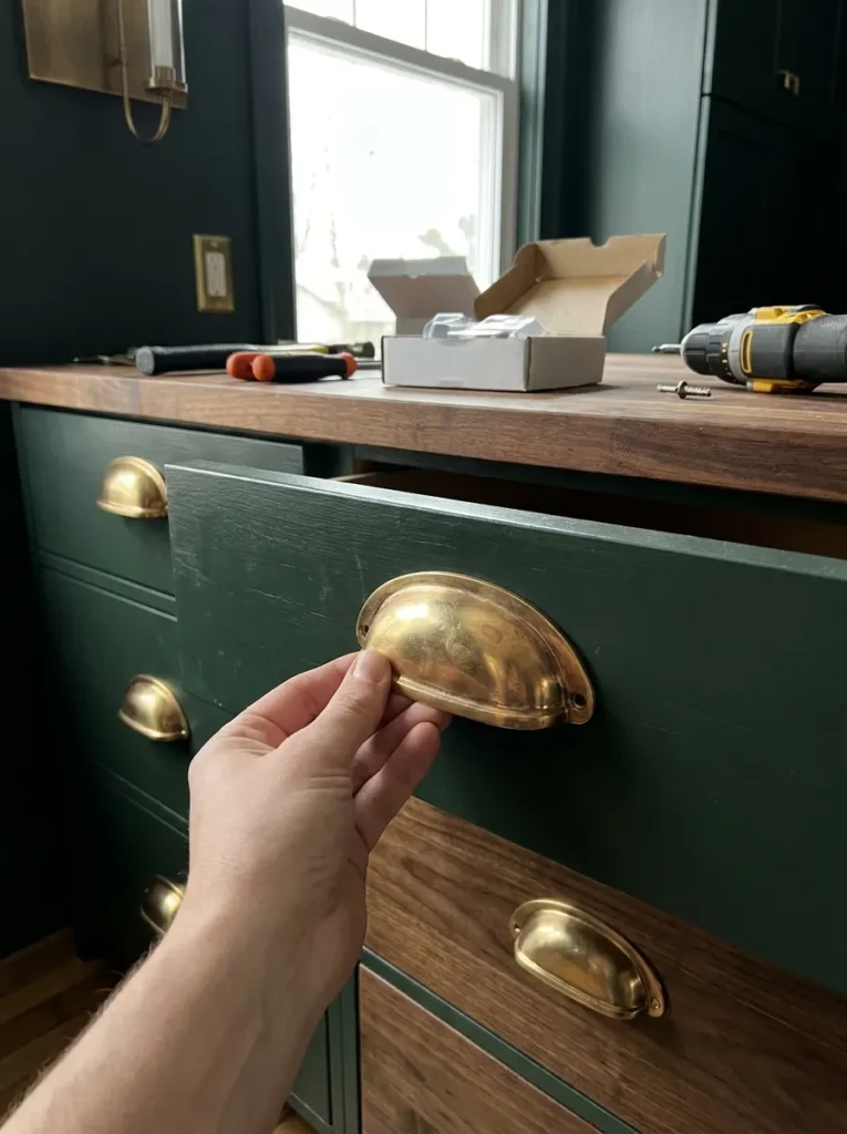 Warm unlacquered brass cup pull on a dark green kitchen drawer