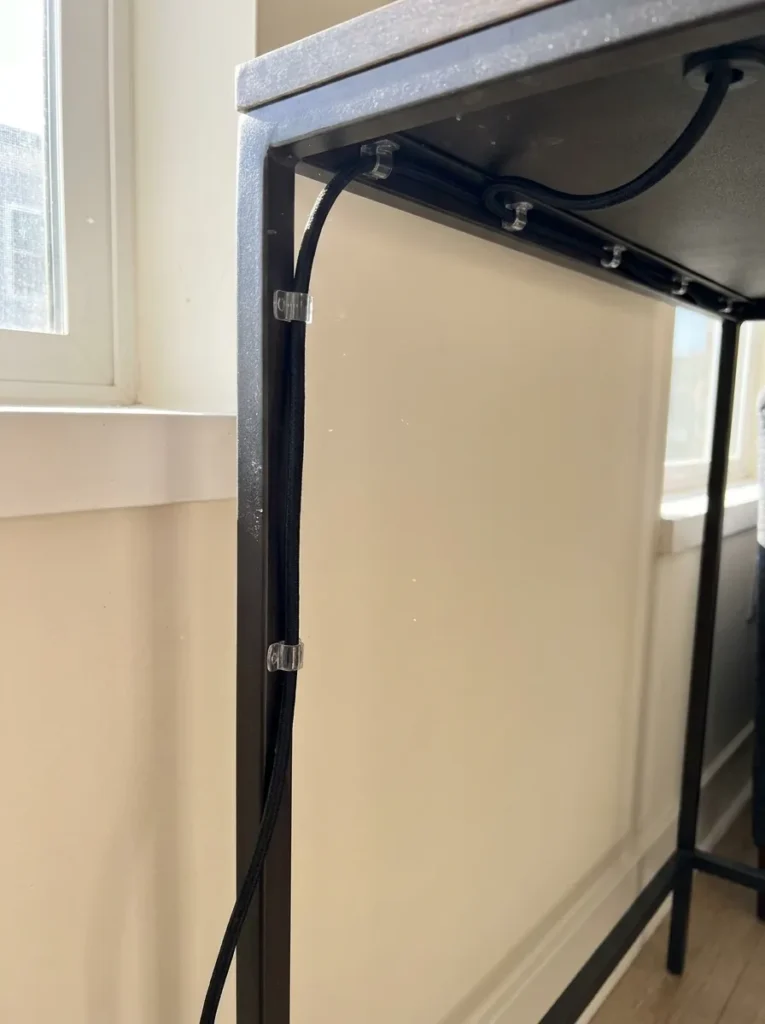 Clear cable clips hiding electrical lamp cords behind a console table leg