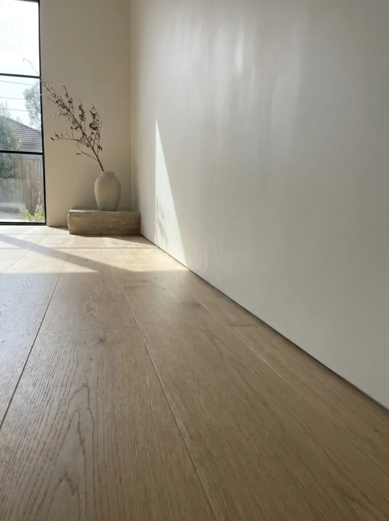 Flush inset baseboard detail where a plaster wall meets oak flooring