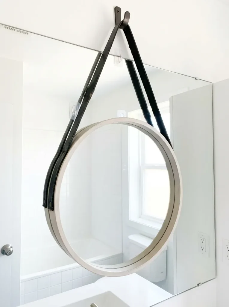 Round mirror with leather strap layered over a flat apartment mirror