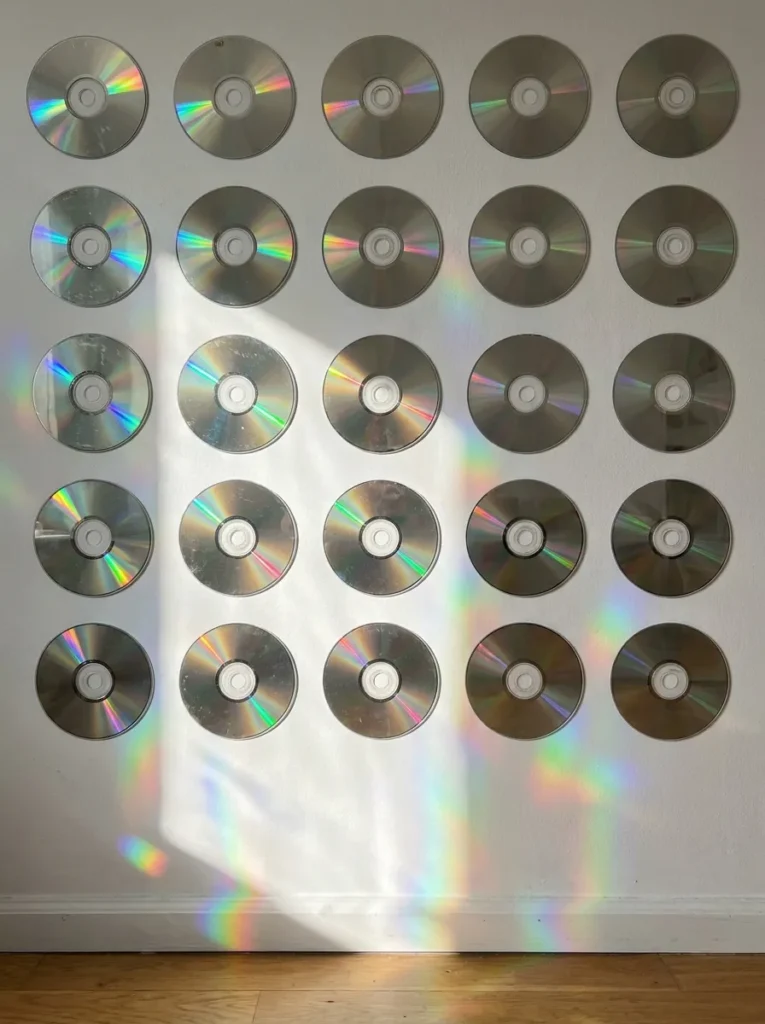 Geometric grid of silver compact discs mounted onto a white wall surface