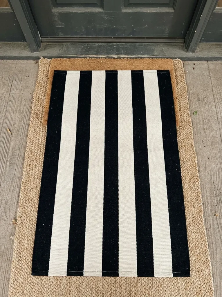 Layered black striped rug over jute mat at a front entrance