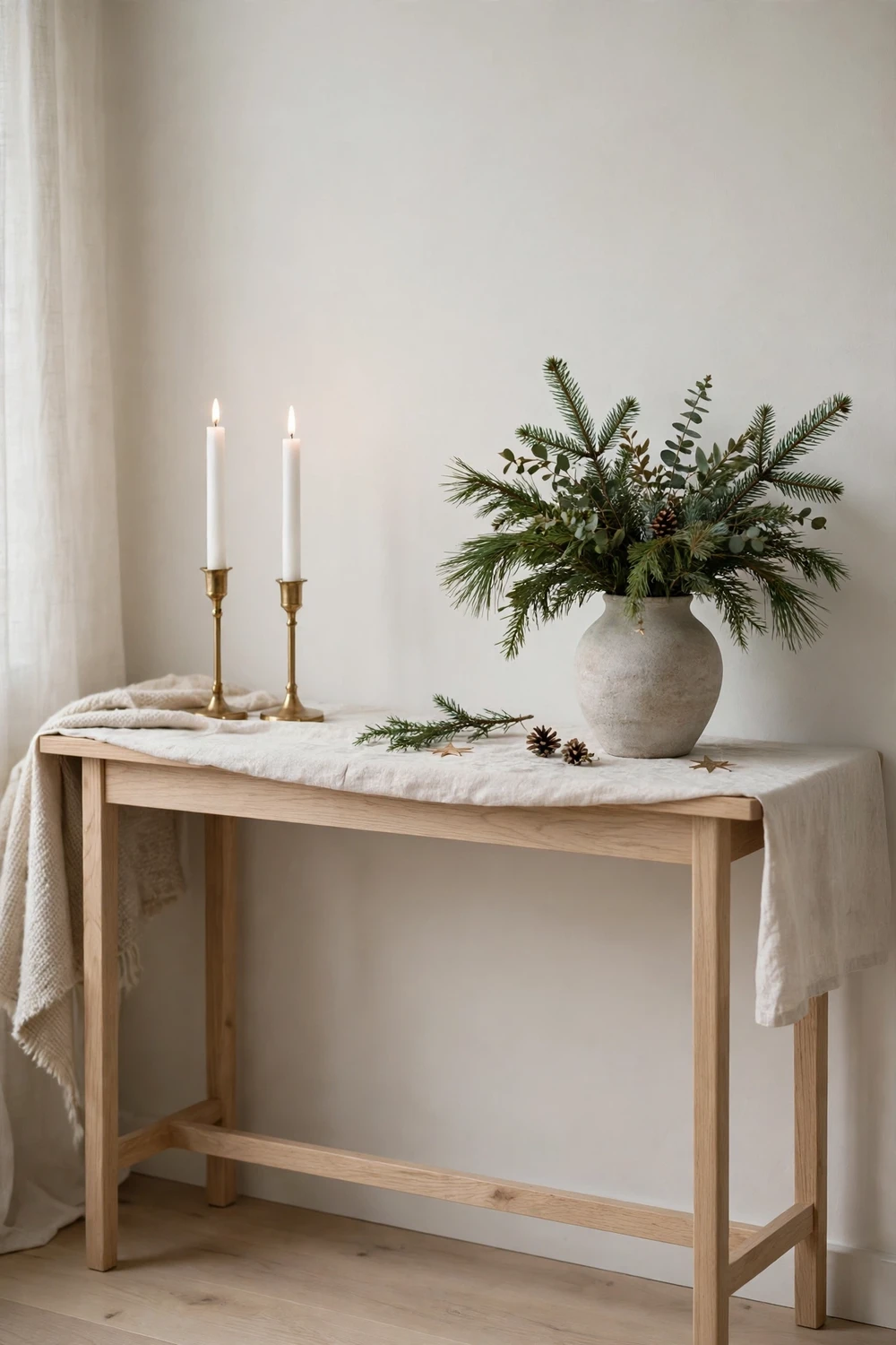 Minimalist Scandinavian console table with tall white candles and evergreen sprigs